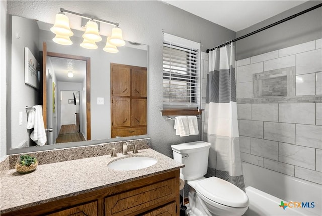 bathroom featuring a textured wall, vanity, toilet, and shower / tub combo with curtain