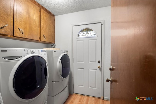 laundry room featuring a textured ceiling, light wood-type flooring, independent washer and dryer, and cabinet space