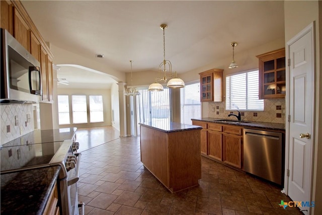 kitchen featuring arched walkways, a sink, glass insert cabinets, appliances with stainless steel finishes, and a center island