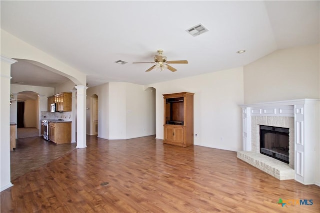 unfurnished living room featuring a ceiling fan, wood finished floors, visible vents, arched walkways, and a brick fireplace