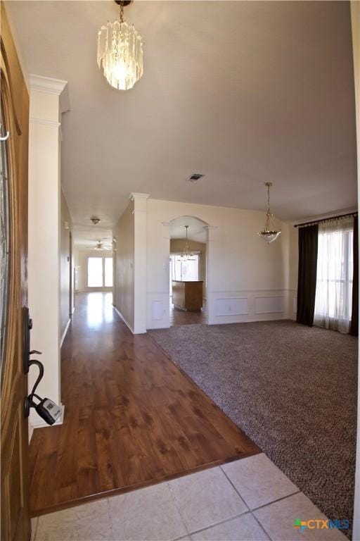 carpeted foyer featuring visible vents, an inviting chandelier, arched walkways, a decorative wall, and a wealth of natural light