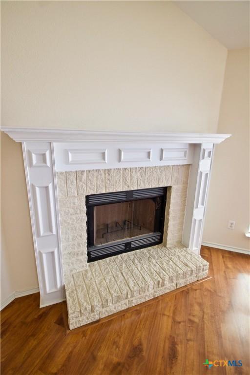 details featuring a brick fireplace, wood finished floors, and baseboards