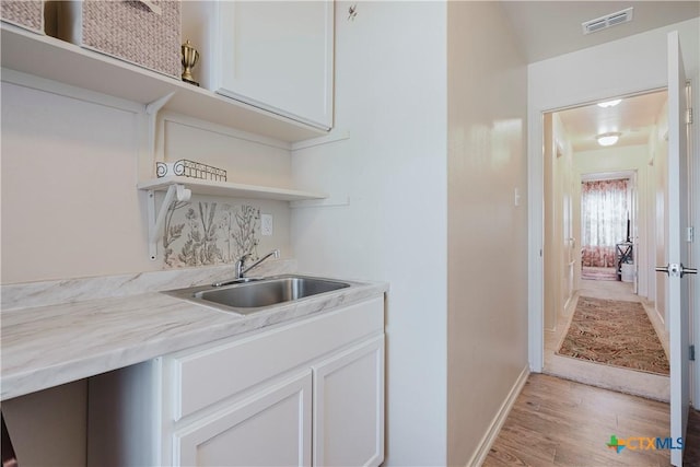 interior space with white cabinetry, sink, light hardwood / wood-style floors, and light stone countertops