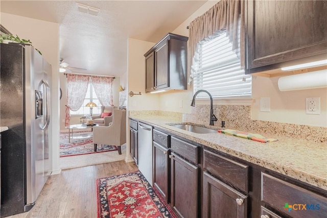 kitchen with appliances with stainless steel finishes, sink, ceiling fan, dark brown cabinets, and light hardwood / wood-style flooring