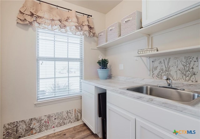 kitchen with white cabinetry, light stone counters, sink, and light hardwood / wood-style flooring