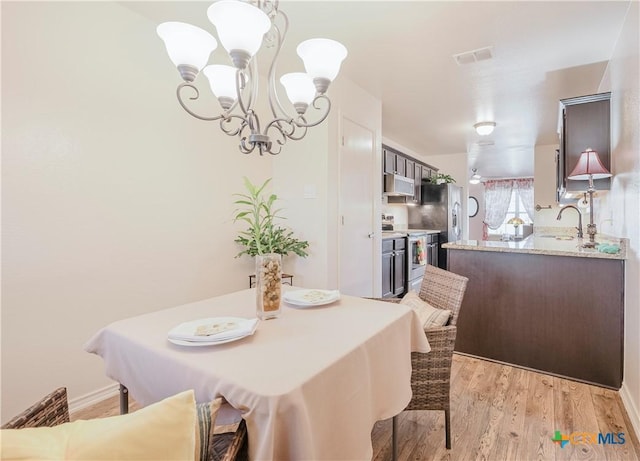 dining space with sink, light hardwood / wood-style floors, and a chandelier