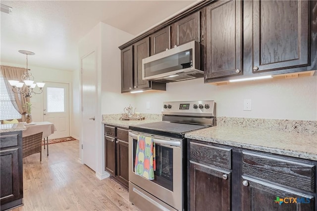 kitchen featuring pendant lighting, stainless steel appliances, light stone countertops, dark brown cabinets, and light wood-type flooring