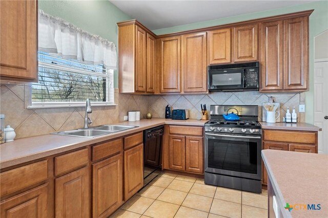 kitchen with black appliances, a sink, tasteful backsplash, light countertops, and light tile patterned floors