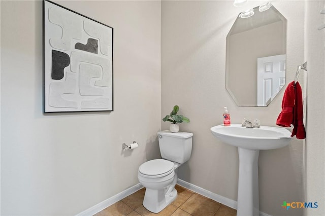 half bathroom featuring a sink, baseboards, toilet, and tile patterned flooring