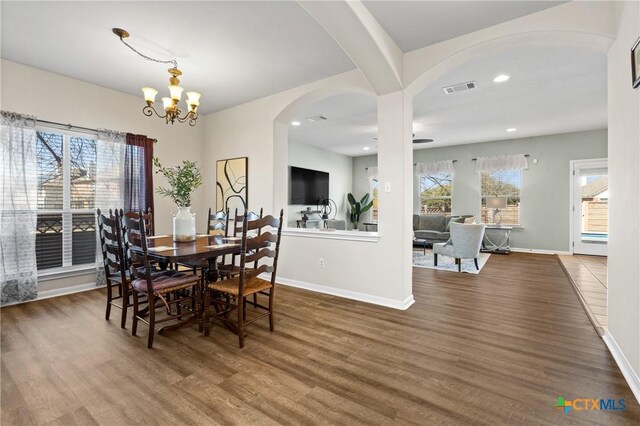 dining room featuring visible vents, a notable chandelier, wood finished floors, arched walkways, and baseboards