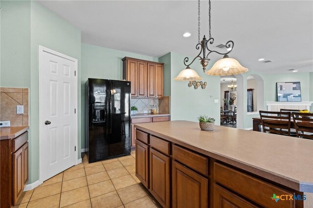 kitchen featuring light tile patterned floors, arched walkways, light countertops, black fridge with ice dispenser, and tasteful backsplash