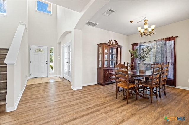 dining space with stairway, visible vents, light wood finished floors, arched walkways, and a notable chandelier