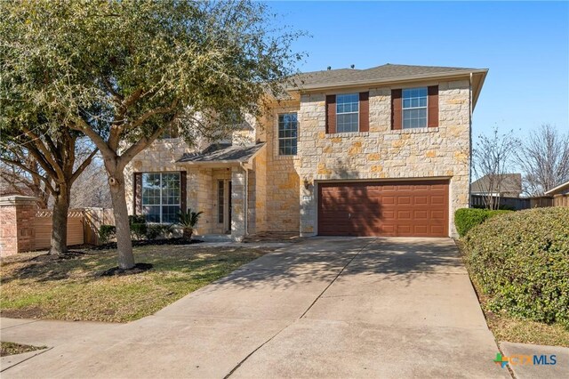 traditional home with stone siding, an attached garage, concrete driveway, and fence