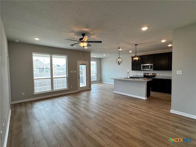 kitchen featuring hardwood / wood-style floors, ceiling fan, a center island with sink, and appliances with stainless steel finishes