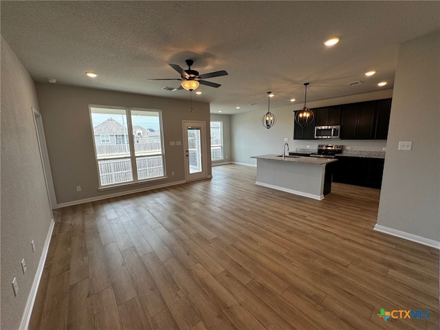 kitchen with stainless steel appliances, a center island with sink, hanging light fixtures, hardwood / wood-style flooring, and sink