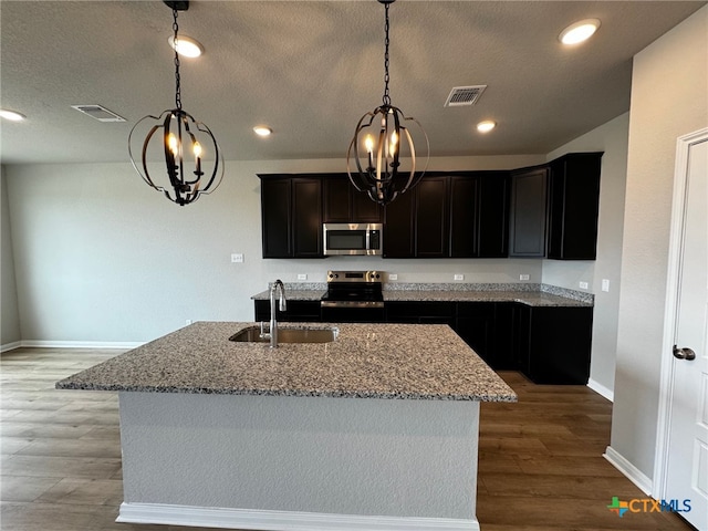 kitchen featuring hardwood / wood-style flooring, sink, an island with sink, light stone countertops, and appliances with stainless steel finishes