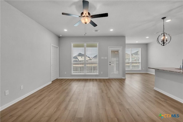 unfurnished living room with ceiling fan with notable chandelier, light hardwood / wood-style floors, and a healthy amount of sunlight