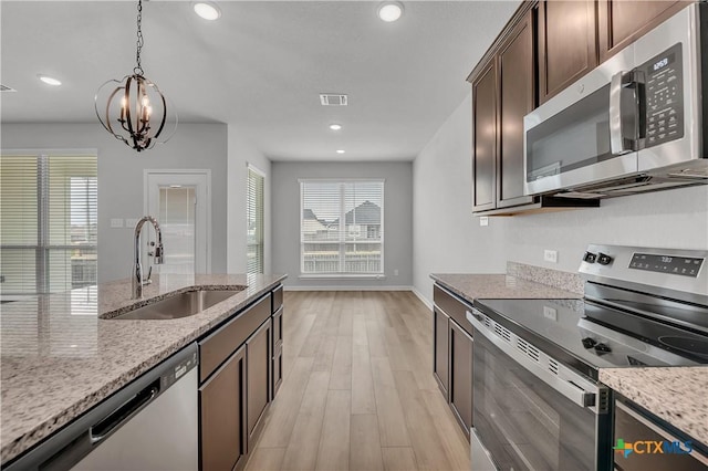 kitchen with dark brown cabinetry, sink, decorative light fixtures, stainless steel appliances, and light stone countertops