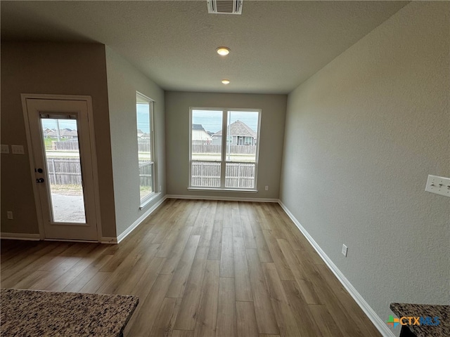 unfurnished dining area featuring a healthy amount of sunlight, light hardwood / wood-style flooring, and a textured ceiling