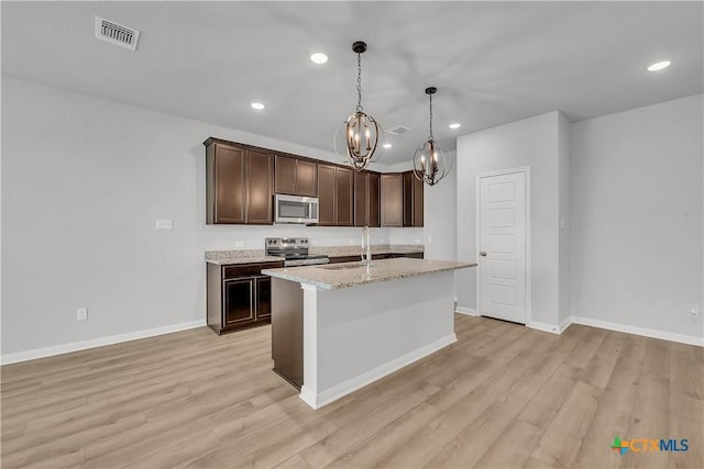 kitchen with appliances with stainless steel finishes, decorative light fixtures, an island with sink, light stone counters, and light wood-type flooring