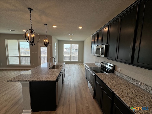 kitchen featuring light hardwood / wood-style floors, stainless steel appliances, sink, a kitchen island with sink, and light stone countertops