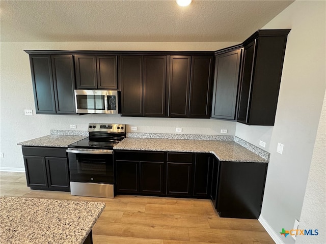 kitchen with light hardwood / wood-style floors, a textured ceiling, and appliances with stainless steel finishes