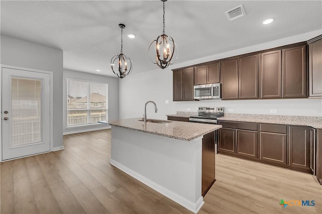 kitchen with sink, hanging light fixtures, stainless steel appliances, light hardwood / wood-style floors, and an island with sink