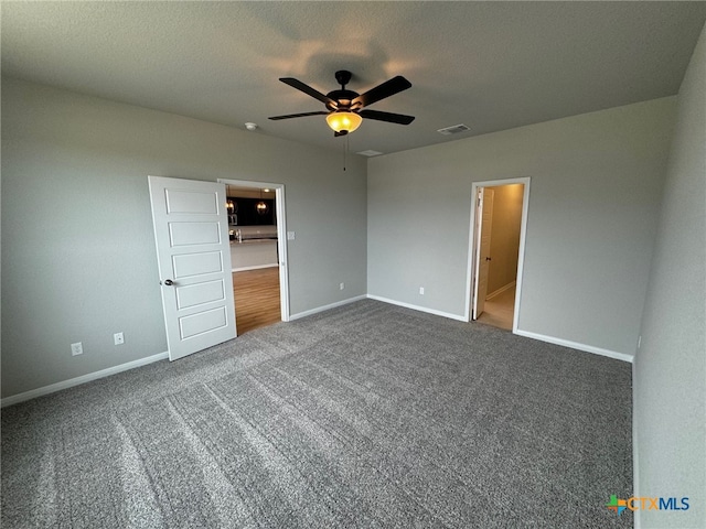 unfurnished bedroom featuring a textured ceiling, dark colored carpet, ceiling fan, and ensuite bathroom