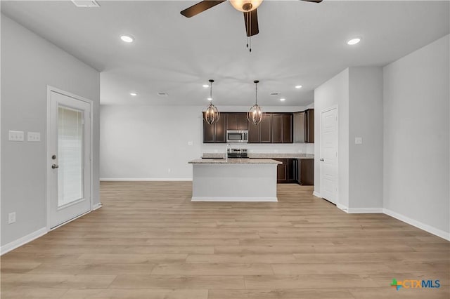 kitchen featuring decorative light fixtures, dark brown cabinets, a center island with sink, light wood-type flooring, and stainless steel appliances