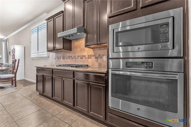 kitchen with crown molding, dark brown cabinets, light tile patterned floors, appliances with stainless steel finishes, and backsplash