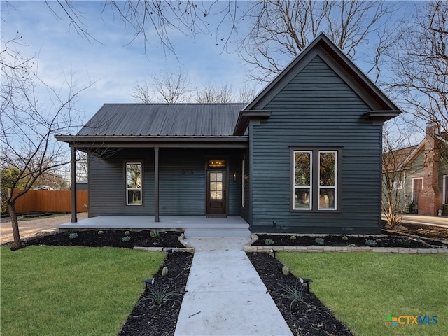 view of front of property with covered porch, metal roof, a front lawn, and fence