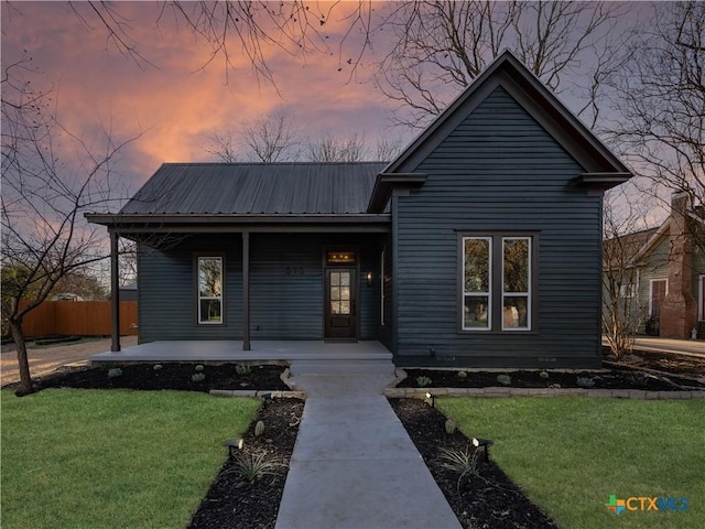 view of front facade featuring a porch, a yard, fence, and metal roof