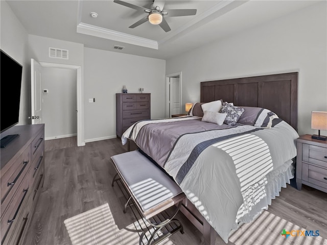 bedroom featuring a raised ceiling, visible vents, baseboards, and wood finished floors