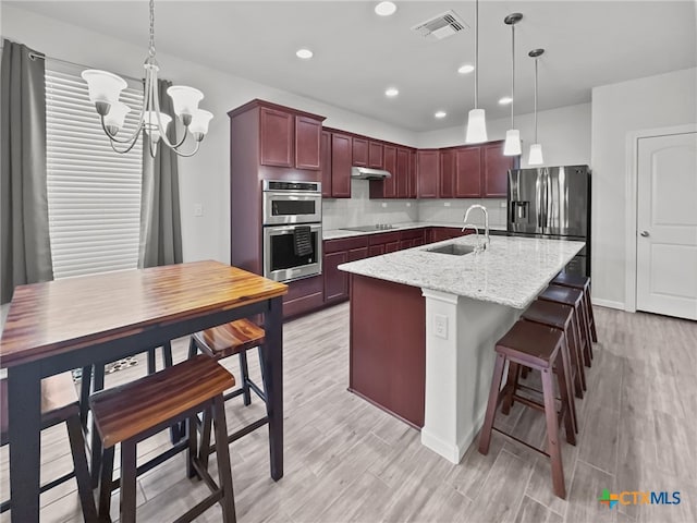 kitchen with a center island with sink, appliances with stainless steel finishes, under cabinet range hood, pendant lighting, and a sink