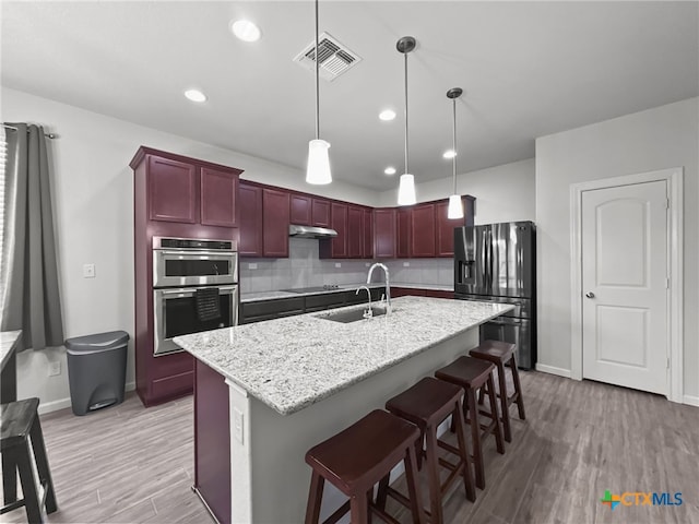 kitchen featuring visible vents, a breakfast bar, decorative light fixtures, stainless steel appliances, and a sink