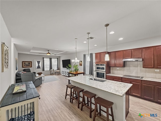 kitchen featuring black electric stovetop, under cabinet range hood, a kitchen breakfast bar, light wood-type flooring, and backsplash