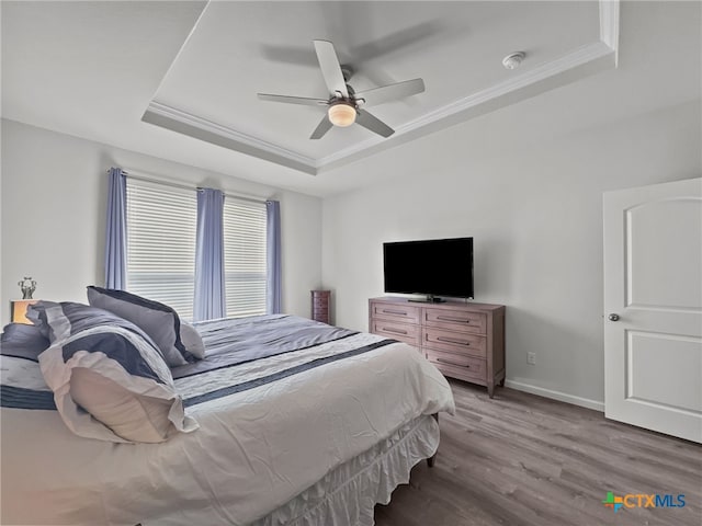 bedroom featuring ornamental molding, light wood-type flooring, a raised ceiling, and baseboards