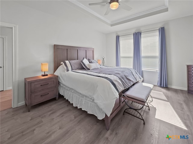 bedroom with a raised ceiling, light wood-style floors, ornamental molding, a ceiling fan, and baseboards