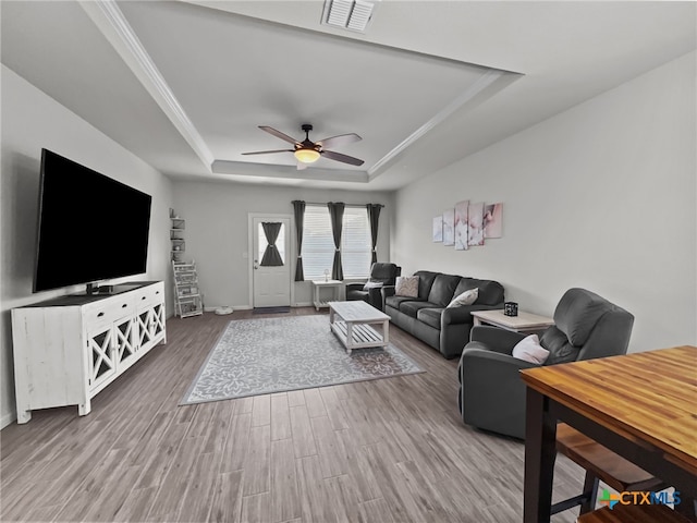 living room featuring a raised ceiling, visible vents, ornamental molding, ceiling fan, and wood finished floors