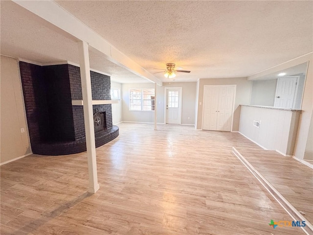 unfurnished living room featuring hardwood / wood-style floors, a textured ceiling, ceiling fan, and a brick fireplace