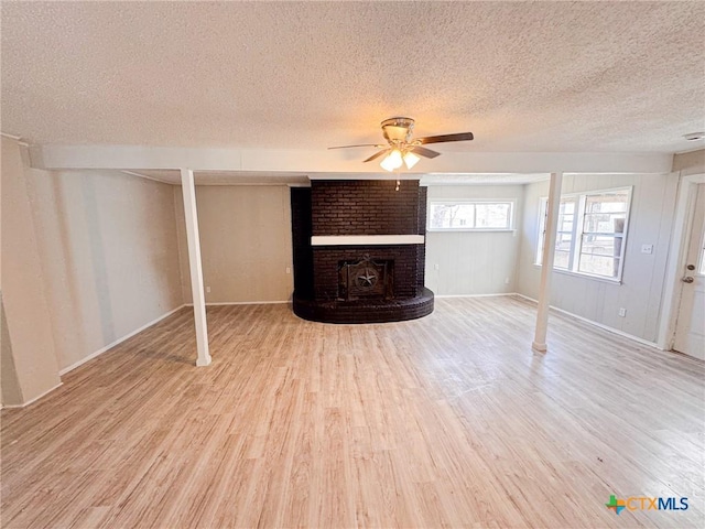 basement featuring a brick fireplace, light hardwood / wood-style floors, a textured ceiling, and ceiling fan