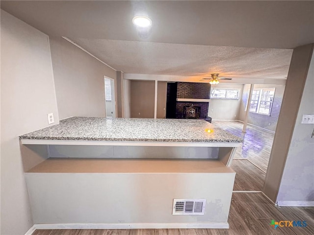 kitchen featuring light stone counters, a brick fireplace, kitchen peninsula, hardwood / wood-style flooring, and ceiling fan