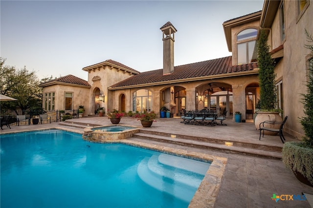 rear view of house with a tiled roof, a patio area, a pool with connected hot tub, and stucco siding