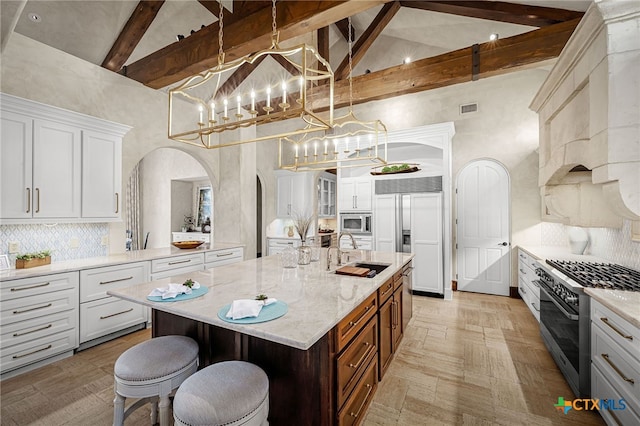 kitchen featuring high vaulted ceiling, arched walkways, a sink, and built in appliances