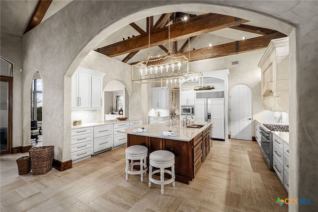 kitchen featuring an island with sink, built in appliances, light countertops, high vaulted ceiling, and beam ceiling