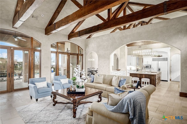 living room featuring a chandelier, arched walkways, beam ceiling, and high vaulted ceiling