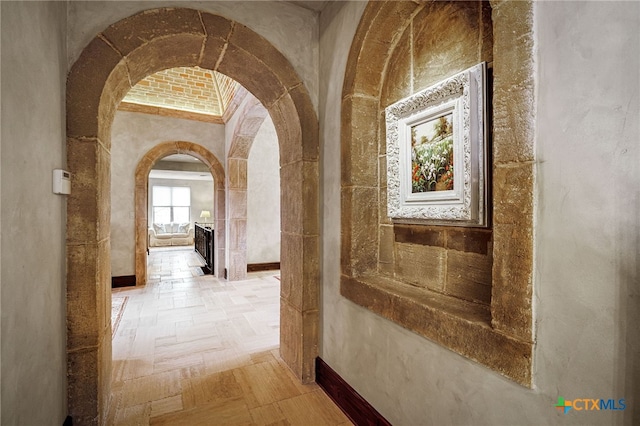 hallway featuring arched walkways and baseboards