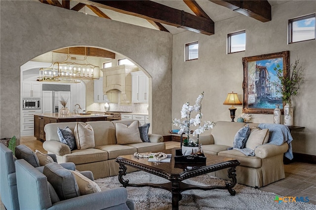 living area with a chandelier, arched walkways, beamed ceiling, and a high ceiling