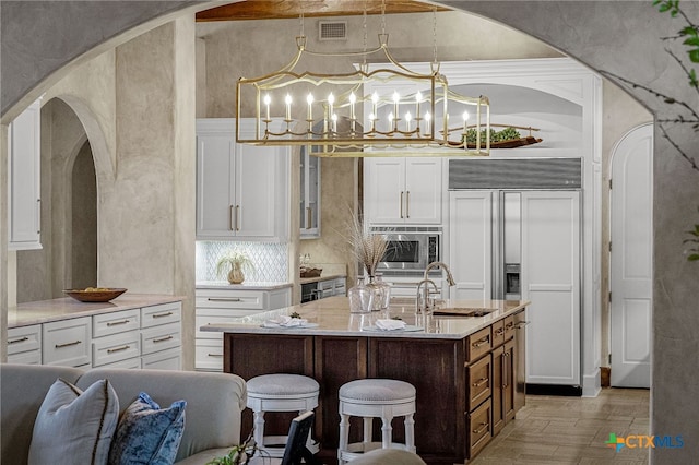 kitchen featuring a center island with sink, visible vents, a sink, built in appliances, and a kitchen bar