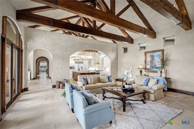 living area featuring arched walkways, visible vents, high vaulted ceiling, beamed ceiling, and baseboards